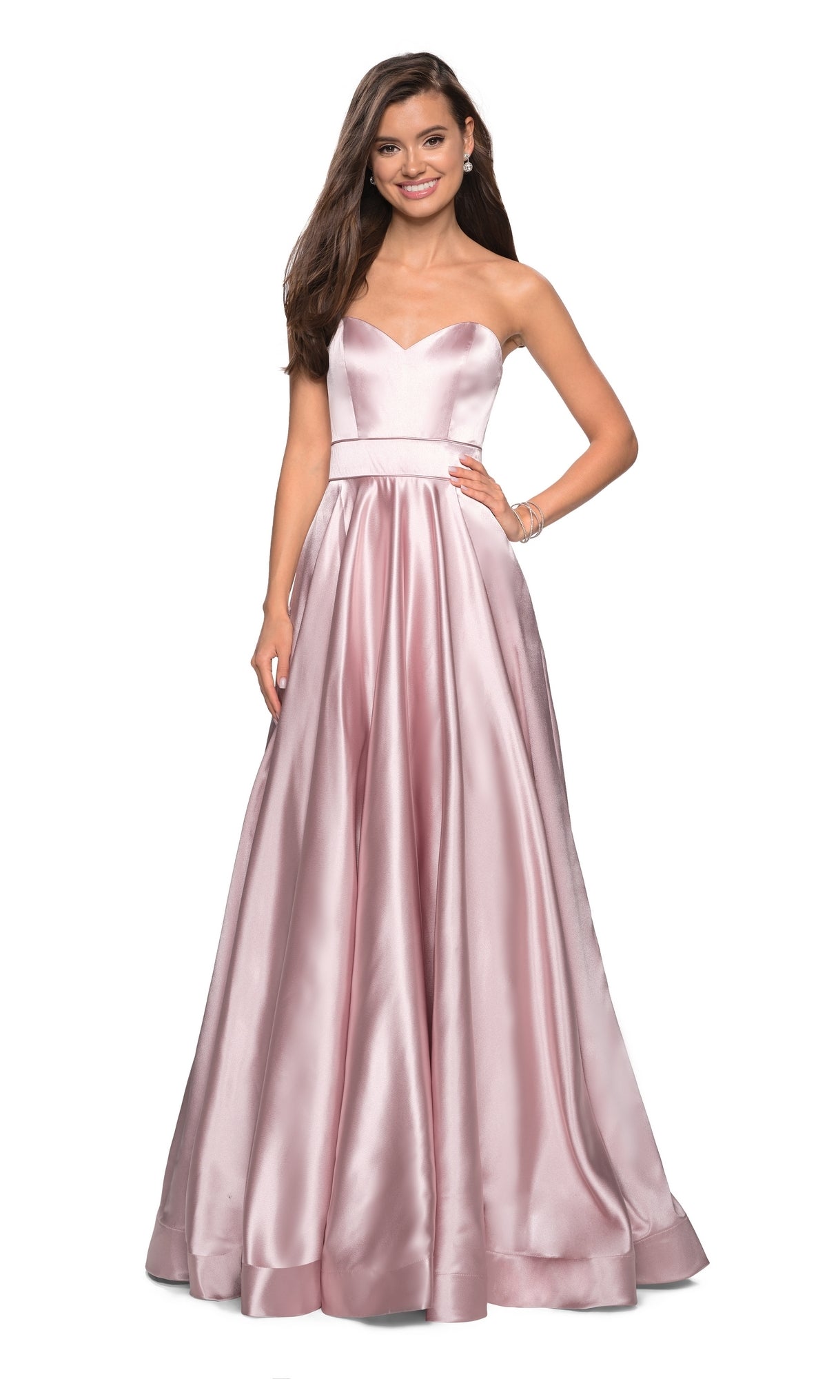 A woman stands smiling in the La Femme 27506 strapless A-line satin prom dress, featuring a fitted bodice and full, floor-length light pink skirt.